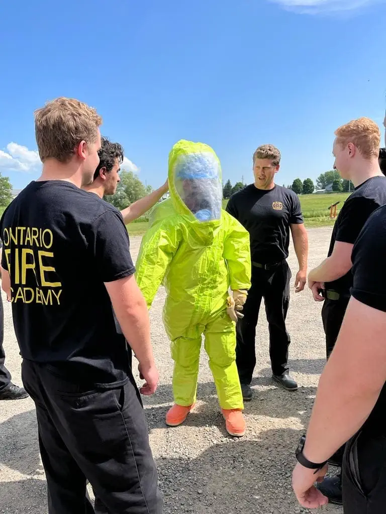 Student in a yellow hazmat suit training with classmates at Ontario Fire Academy