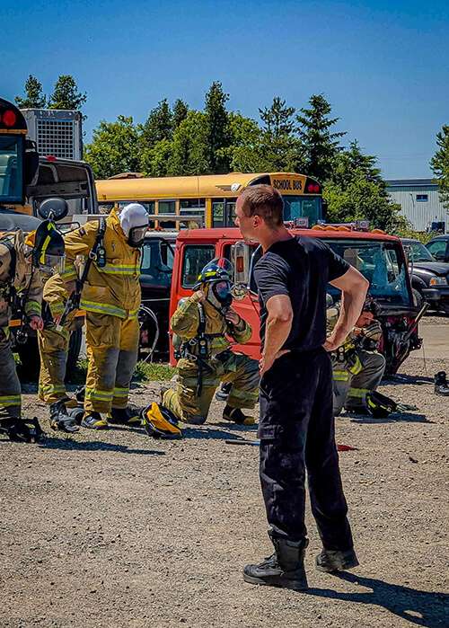 Instructor supervising firefighter recruits during a vehicle extrication training exercise