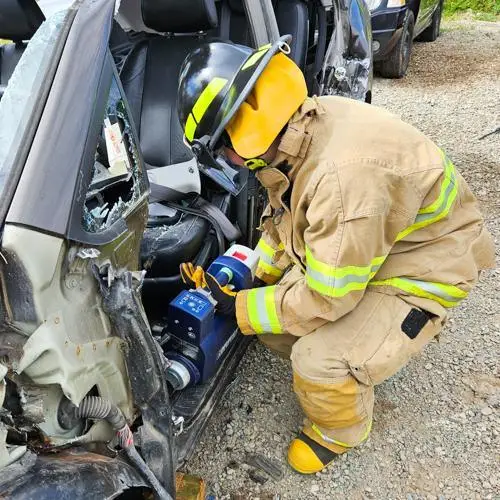 Firefighter recruit using extrication tools on a wrecked vehicle during training