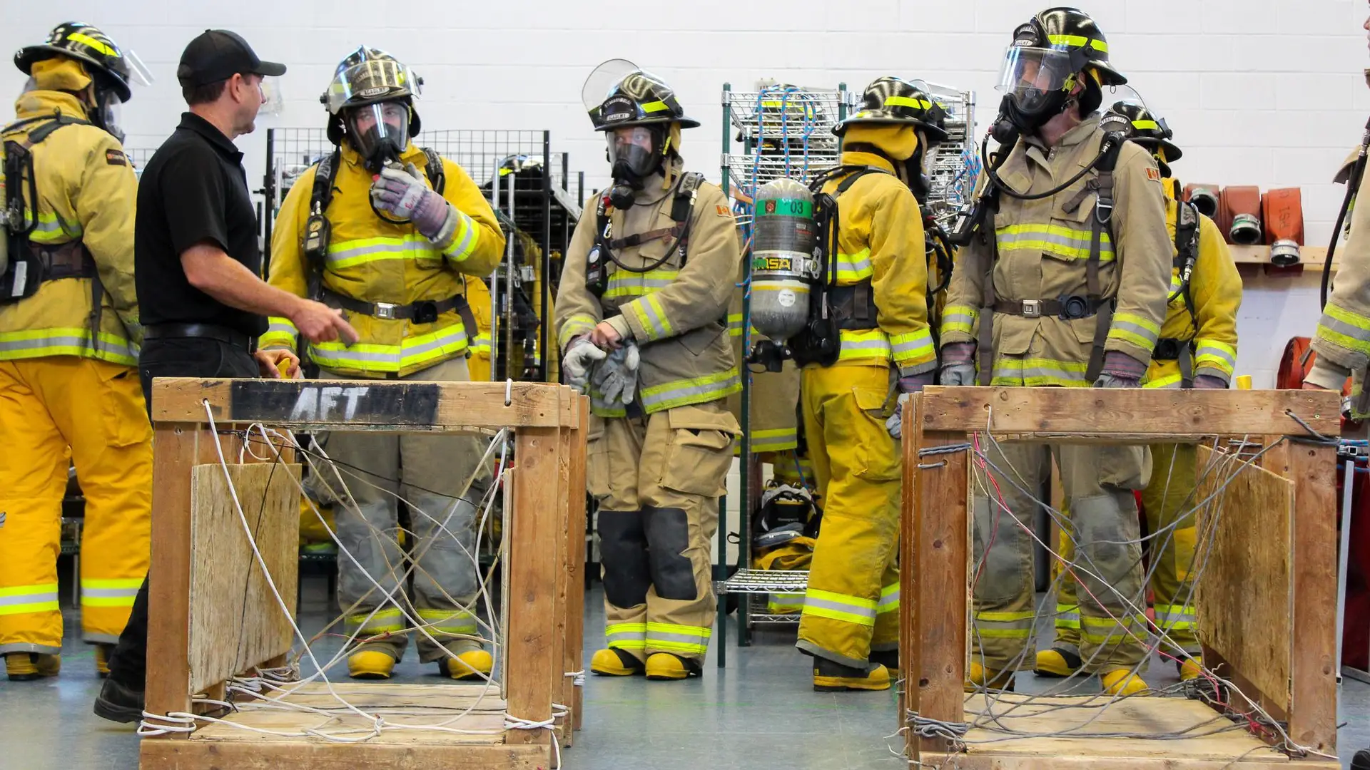 Instructor briefing firefighter recruits wearing SCBA gear during indoor training